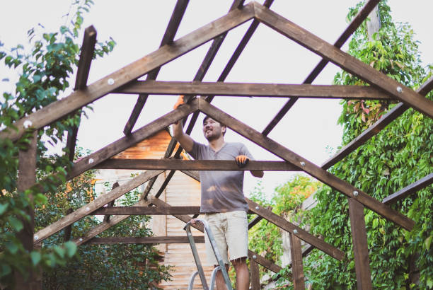 Man building wooden roof outdoors standing on ladder.