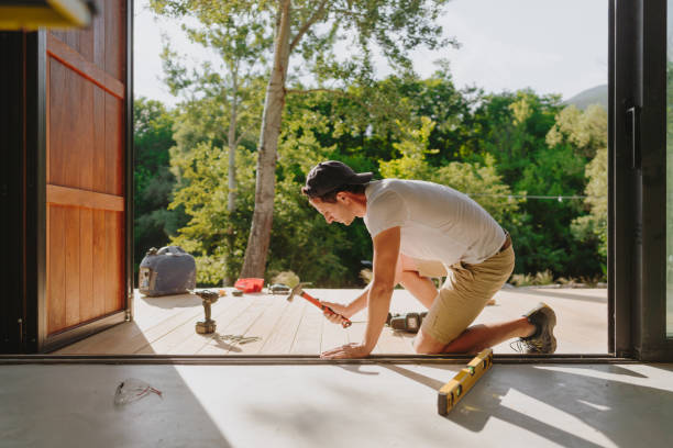 Photo of a carpenter installing wooden decking in front of a cabin house