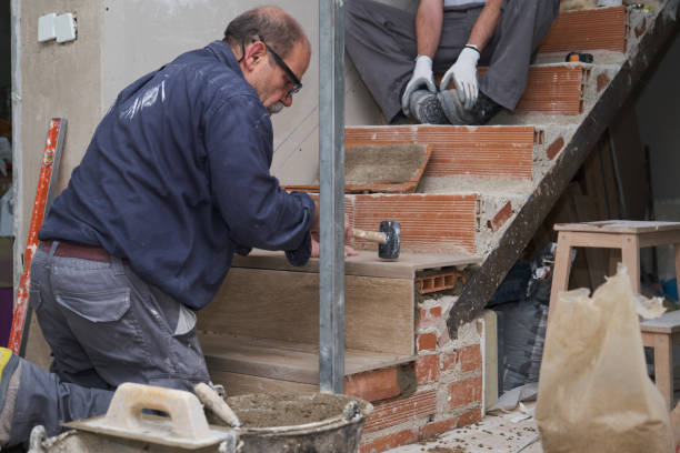 Senior bricklayer building a ceramic wood effect staircase in a home interior. House renewal.